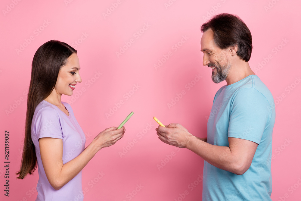 Profile portrait of two cheerful people use telephone write comment isolated on pink color background Profile portrait of two cheerful people use telephone write comment isolated on pink color background