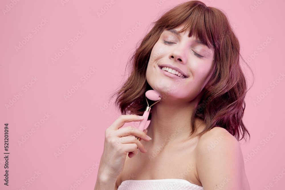 happy woman standing on a pink background with pink lighting from the side, with beautiful, wave-styled hair, closing her eyes with pleasure while doing a facial massage with a pink roller happy woman standing on a pink background with pink lighting from the side, with beautiful, wave-styled hair, closing her eyes with pleasure while doing a facial massage with a pink roller
