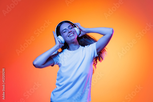 Portrait of adorable young girl, student wearing casual style clothes isolated on orange color background in neon light. Concept of beauty, art, fashion, emotions