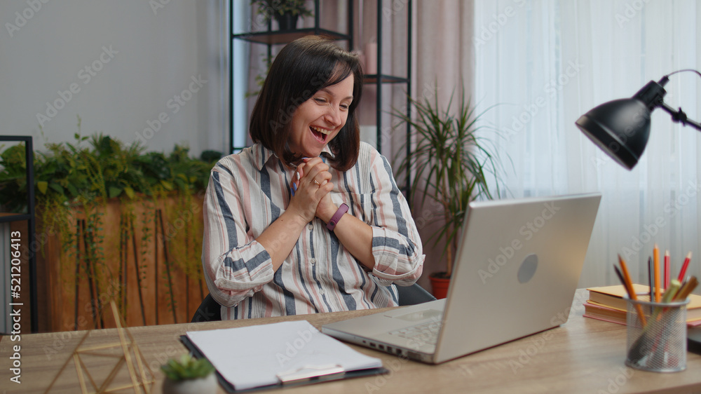 Overjoyed young woman freelancer at home office working with laptop scream in delight raise hands in triumph winner gesture celebrate success win money in lottery. Excited girl get online good news Overjoyed young woman freelancer at home office working with laptop scream in delight raise hands in triumph winner gesture celebrate success win money in lottery. Excited girl get online good news