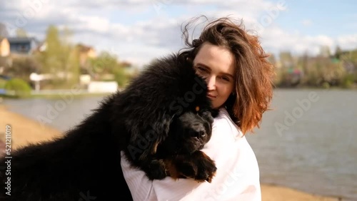 Smiling woman hugging tibetan mastiff dog looking at camera outdoors. Girl and dog playing on the beach photo