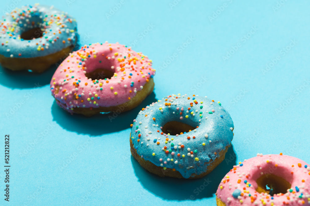 High angle close-up view of donuts with sprinklers in row on blue background High angle close-up view of donuts with sprinklers in row on blue background