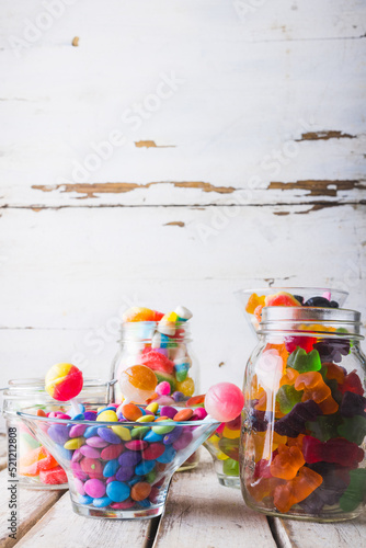 Close-up of multi colored various candies and lollipops in glass jars and bowl on table