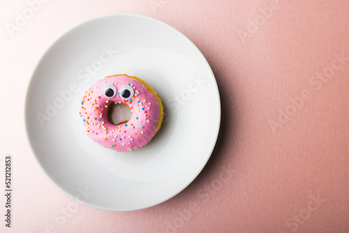 Directly above view of fresh donut with googly eyes in white plate by copy space on pink background