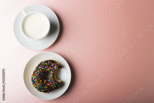 Overhead view of chocolate donut in plate by cup of milk and copy space on colored background