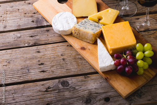 High angle view of various cheese with grapes on wooden board at table, copy space