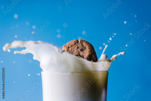 Close-up of spilled milk with cookie in glass against blue background, copy space