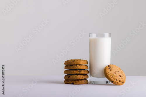Milk in glass by cookies against white background, copy space