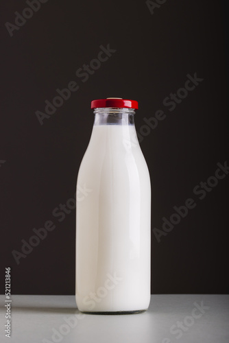 Milk in glass bottle on table against black background with copy space