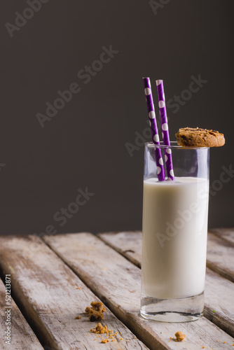 Milk glass with straws and cookie on table against gray background, copy space