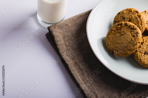 Cookies in plate by milk glass on white background, copy space