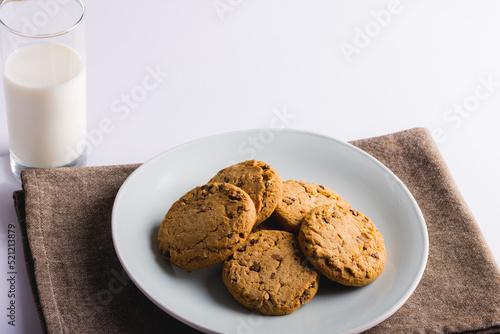 Cookies in plate by milk glass on white background with copy space