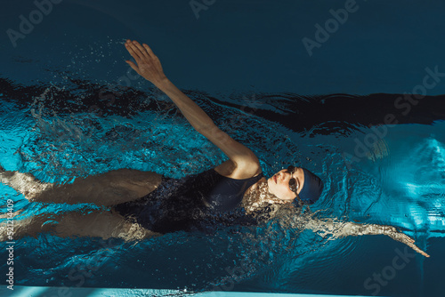 Картината върху платно From above of professional female swimmer in swimsuit goggles and cap doing back