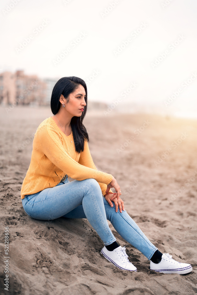 portrait of a young latin woman sitting on the beach looking at tthe horizon over the ocean