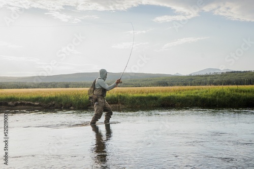 Fotografia Side view of fisherman in a hoodie in the lake with the rod in the air