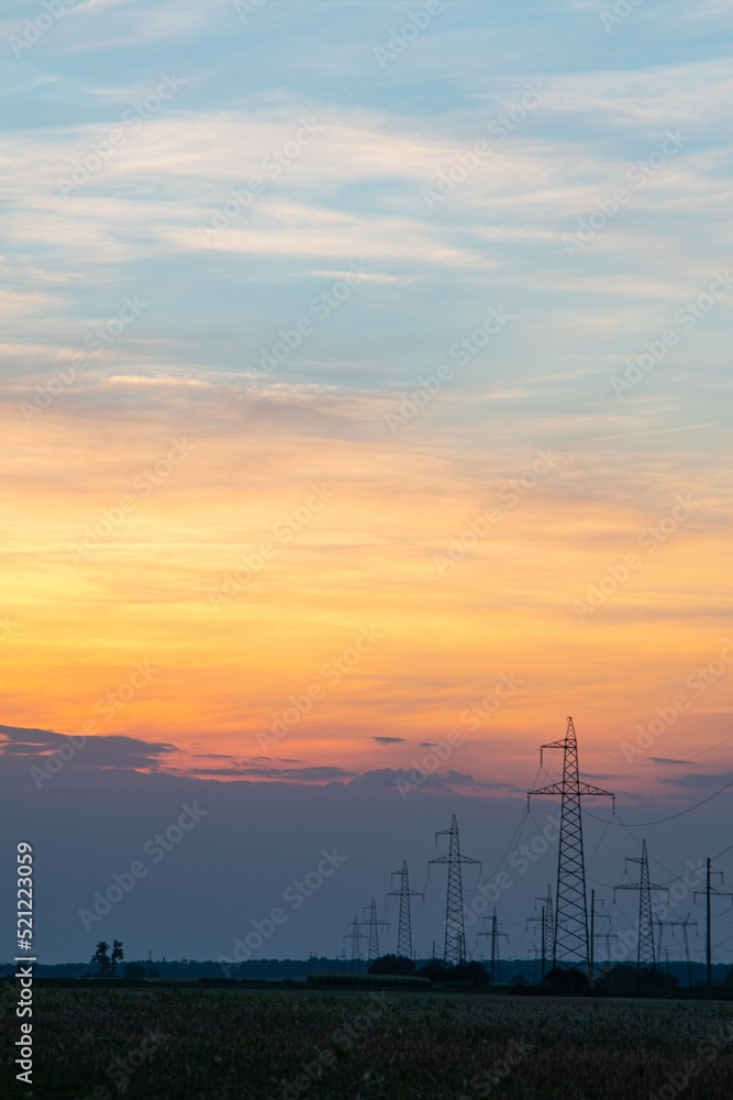A high-voltage tower in the middle of a wheat field, against the background of a warm summer sunset