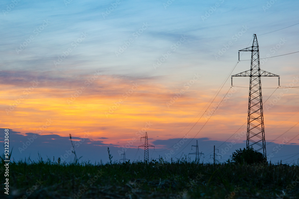 A high-voltage tower in the middle of a wheat field, against the background of a warm summer sunset