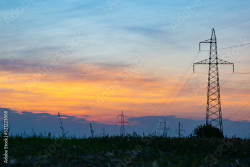 A high-voltage tower in the middle of a wheat field, against the background of a warm summer sunset © ArtozS