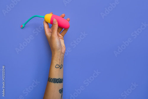Tattooed girl holding vibrating egg for clitoral stimulation over violet wall background