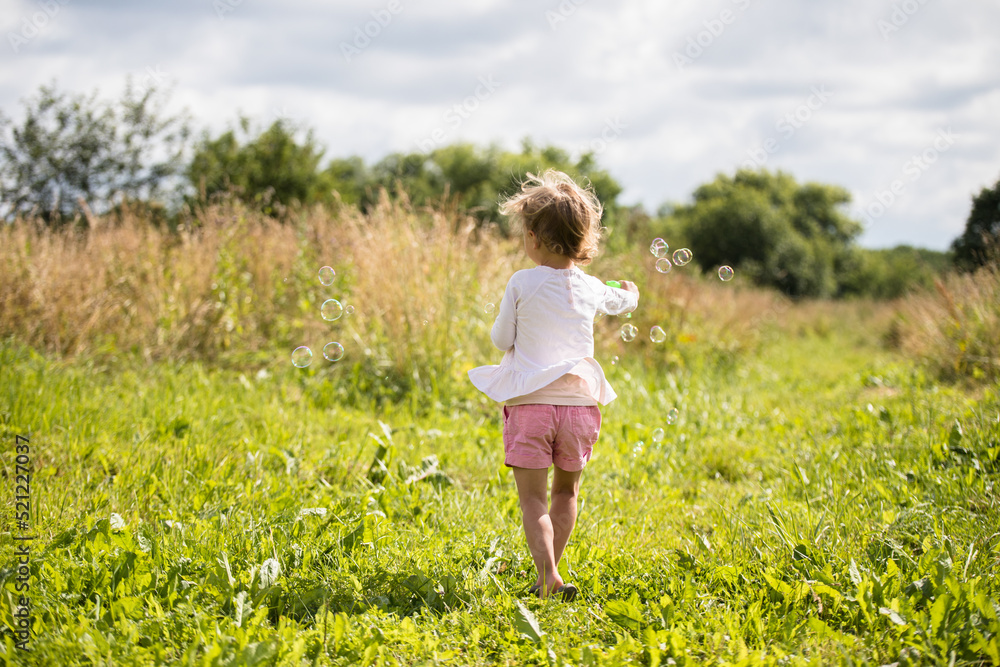 Beautiful little girl, has happy fun cheerful smiling face, soap bubble blower.