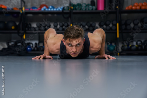 Muscular man doing push up exercises during intense fitness workout in grungy gym