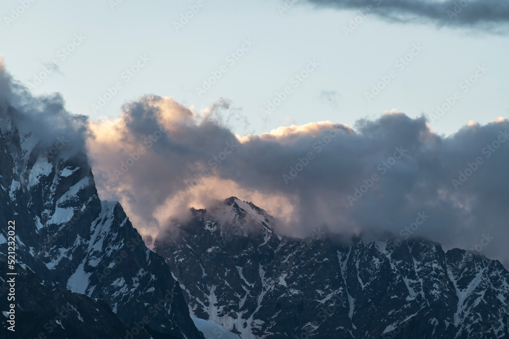 Beautiful mountains landscape on the sunset. High snow covered mountains in the fog and clouds.