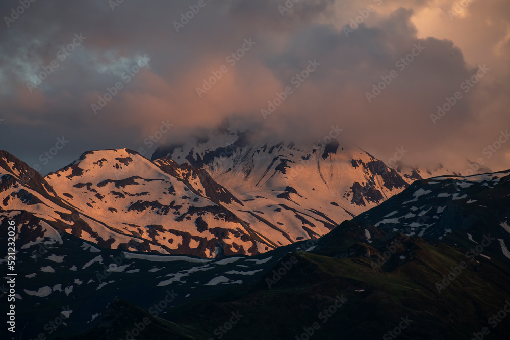 Beautiful mountains landscape on the sunset. High snow covered mountains in the fog and clouds.