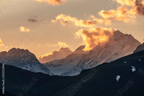 Beautiful mountains landscape on the sunset. High snow covered mountains in the fog and clouds. 
