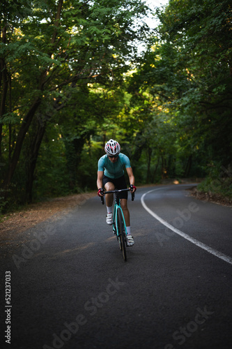 Professional female cyclist trains in the woods. Woman riding race bicycle on a forest asphalt road, uphill, front view