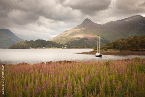 Boat sailing in a lake against a green field and mountains on a cloudy day in Glencoe, Scotland photo