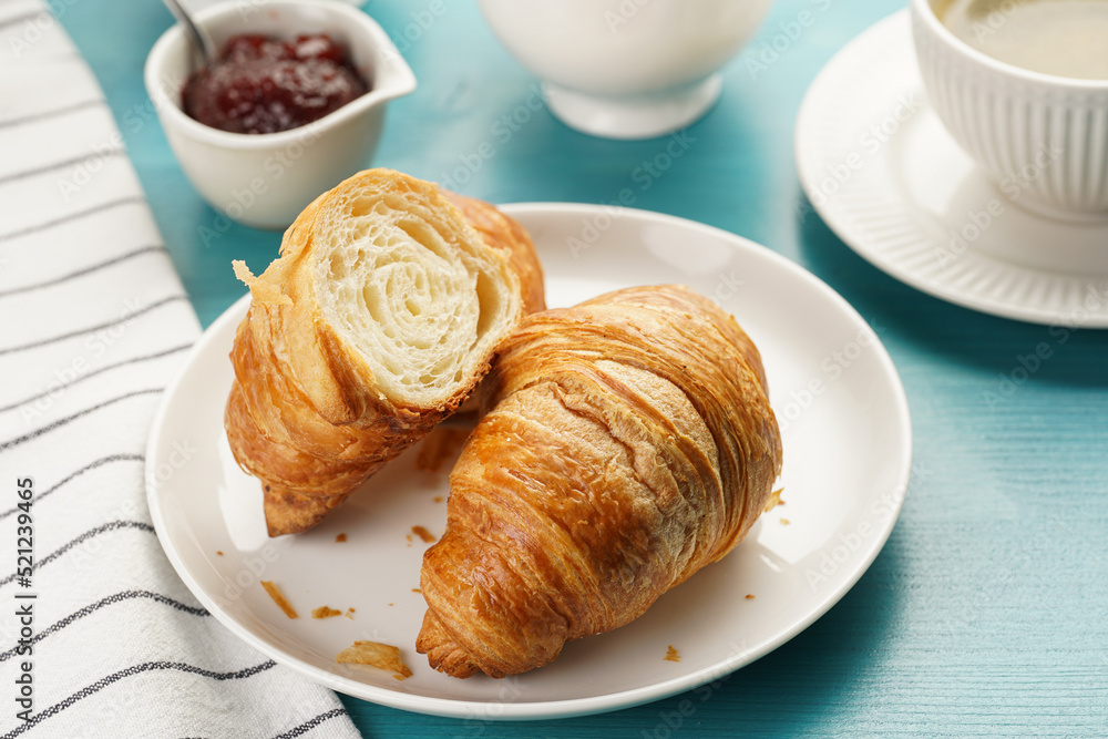 Two french soft croissants on a white plate on a blue wooden table, a cup of black coffee in white sophisticated cup, milk, sugar, jam Two french soft croissants on a white plate on a blue wooden table, a cup of black coffee in white sophisticated cup, milk, sugar, jam