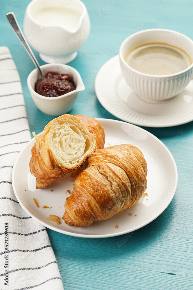 Two french soft croissants on a white plate on a blue wooden table, a cup of black coffee in white sophisticated cup, milk, sugar, jam Two french soft croissants on a white plate on a blue wooden table, a cup of black coffee in white sophisticated cup, milk, sugar, jam