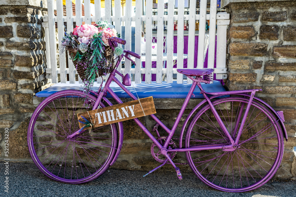 Old Vintage Bicycle Painted In Purple With Flower Basket For Decoration In Front Of A White Fence Of A Bistro