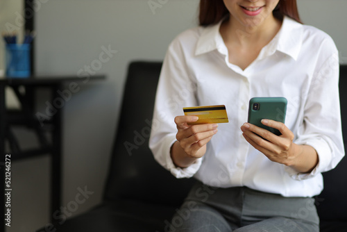 Asian woman sitting on sofa at home using smartphone to send text messages. Concept for using credit cards and shopping online from home. © Wasan