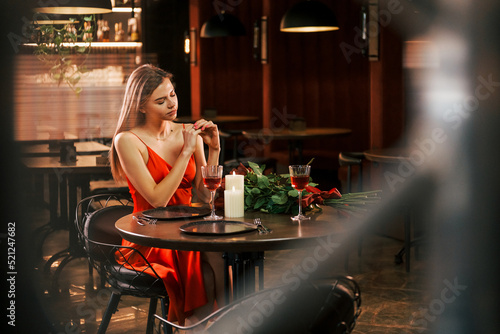 Woman in red dress sitting alone in the restaurant. Flowers and candles