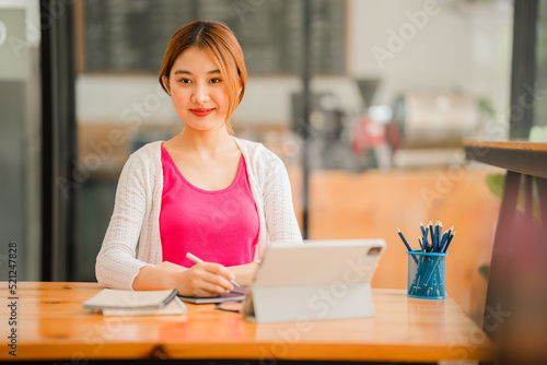 Happy Asian female student wearing headphones, studying online, watching webinars, podcasts on tablets, listening, learning, education courses. online meeting