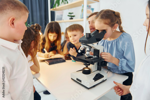 Girl looking into microscope. Group of children students in class at school with teacher