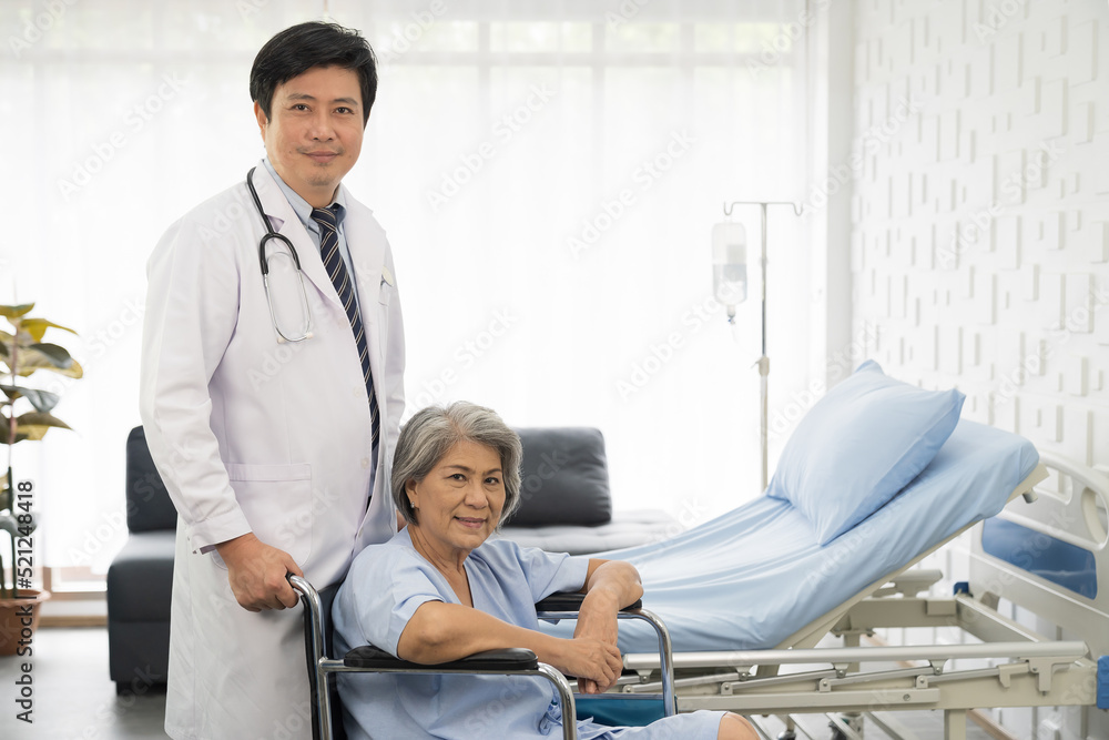 Obraz premium Portrait of male doctor and elderly patient woman sit on wheelchair. Male doctor visit or taking care elderly asian woman on wheelchair at the hospital. People and health care concept