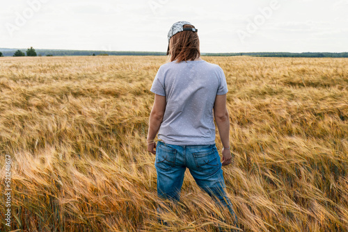 Rear view woman in jeans among yellow dry cereal wheat field agriculture and grain harvest Mockup friendly © Lena_viridis