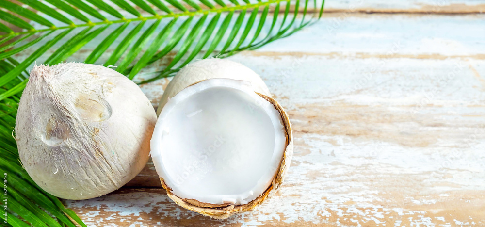 A fresh coconut with husks cut in half revealing white coconut flesh and coconut leaves on an old wooden background. A fresh coconut with husks cut in half revealing white coconut flesh and coconut leaves on an old wooden background.