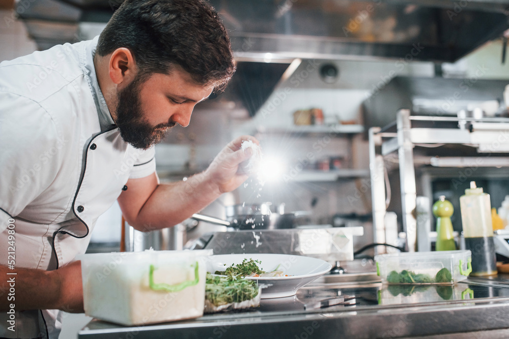 Fototapeta premium Man poring some salt. Professional chef preparing food in the kitchen