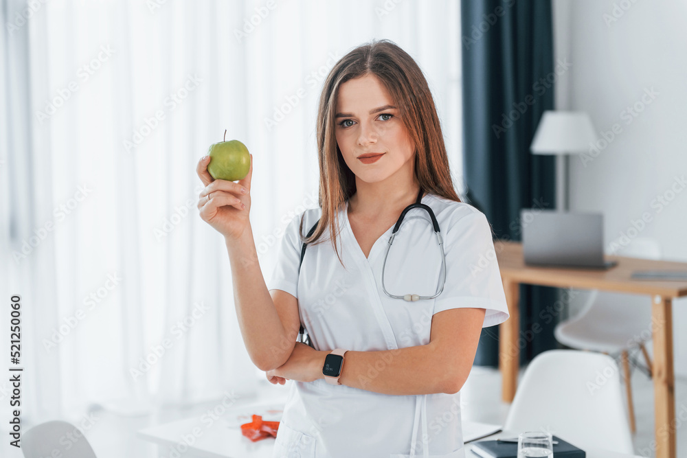 Woman holding an apple. Professional medical worker in white coat is in the office