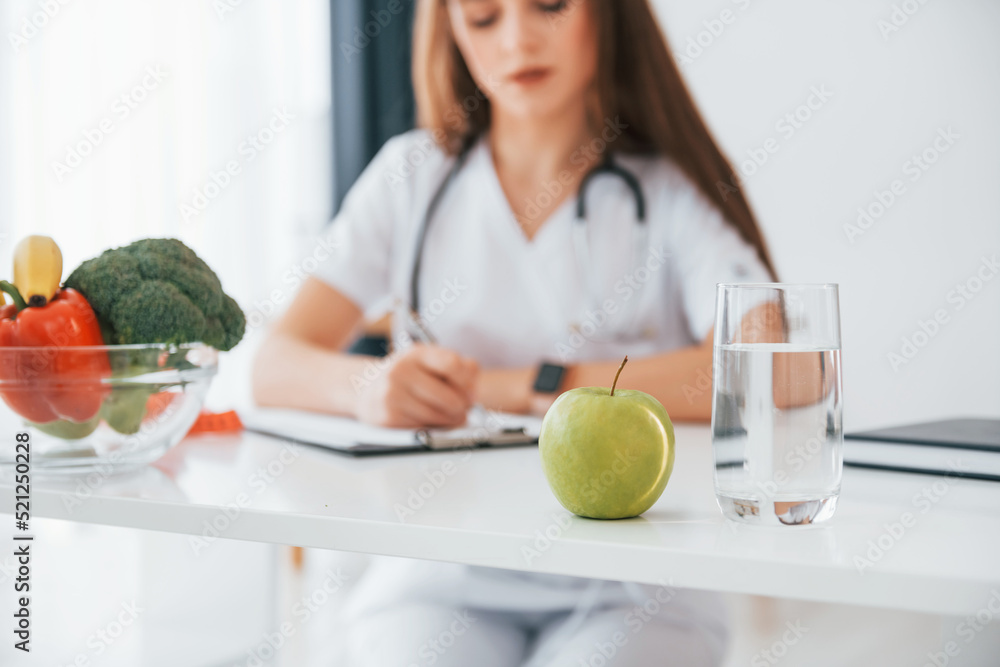 Woman writing information into the notepad. Professional medical worker in white coat is in the office