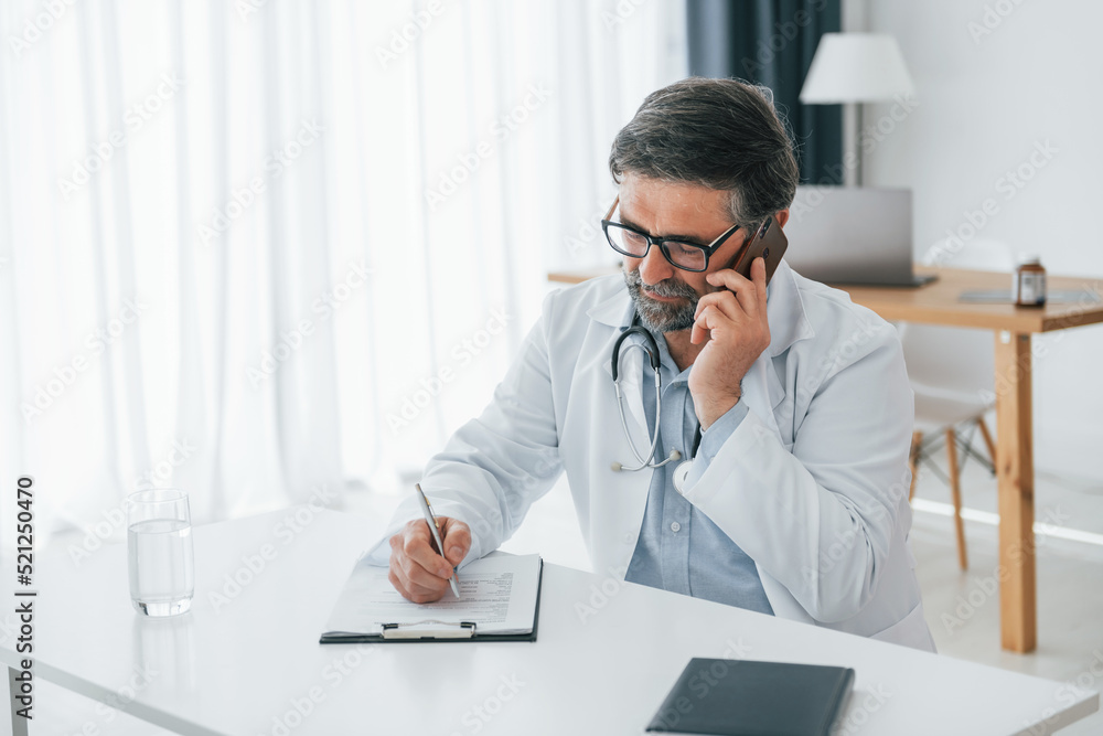Man giving information by phone. Professional medical worker in white coat is in the office Man giving information by phone. Professional medical worker in white coat is in the office