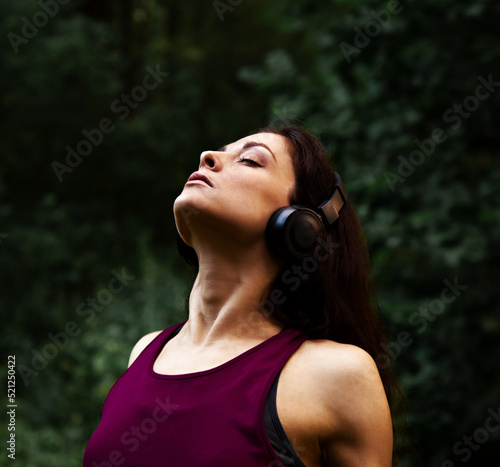 Sporty beautiful young woman training outdoors summer green forest evening background and listening the music in headphone with relaxing closed calm eyes. Closeup
