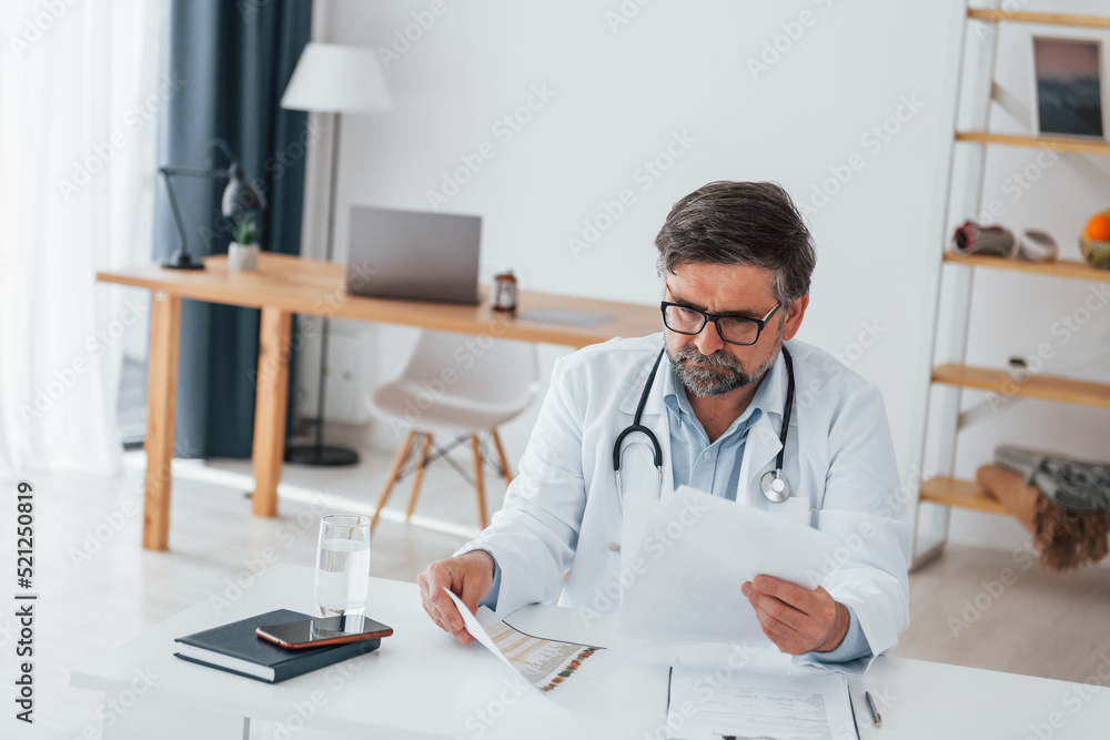 Man is busy with documents. Professional medical worker in white coat is in the office Man is busy with documents. Professional medical worker in white coat is in the office