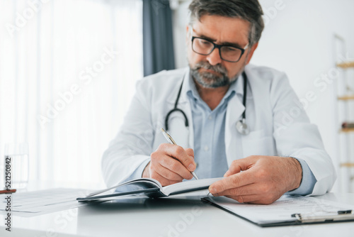 Man is working with documents. Mature doctor in white coat is in the office