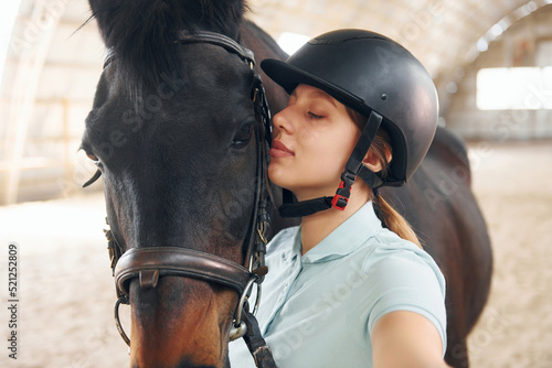 Making lovely selfie. A young woman in jockey clothes is preparing for a ride with a horse on a stable