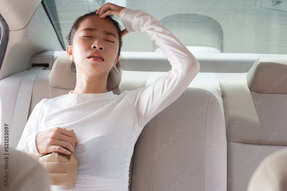 An Asian woman has car sickness holding a vomit bag and trying to recover from the pain of car sickness, nausea, and vomiting - obrazy, fototapety, plakaty 