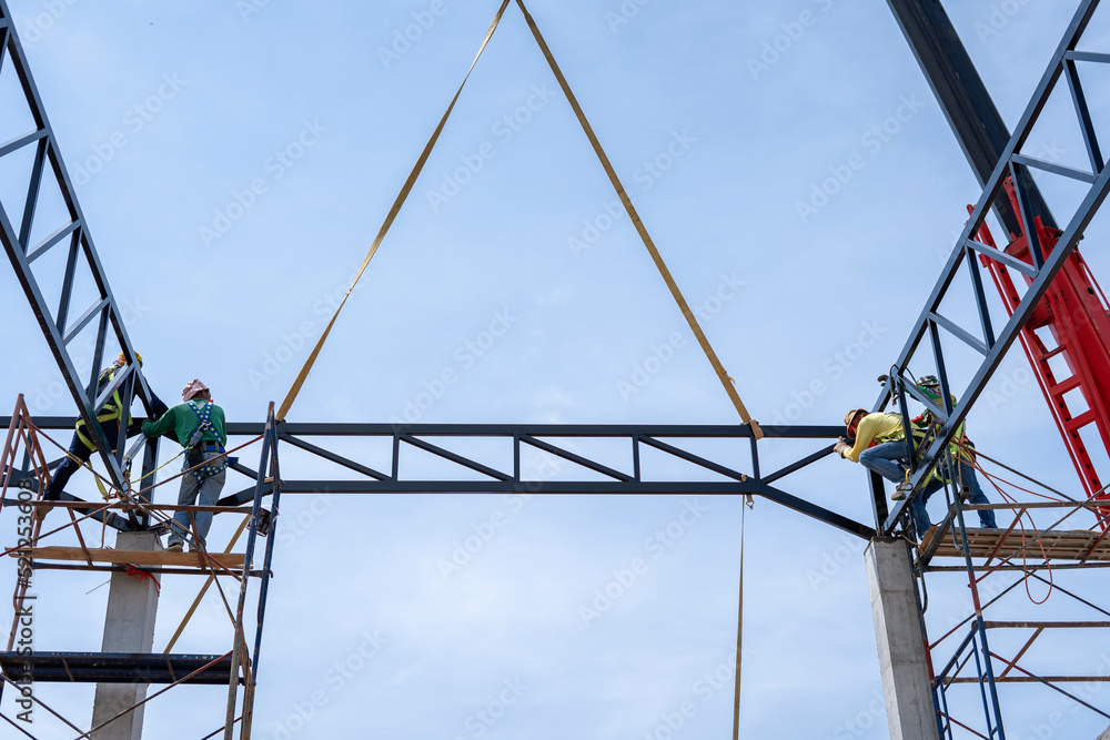 Construction workers wear safety belts to install steel trusses to weld roof trusses.